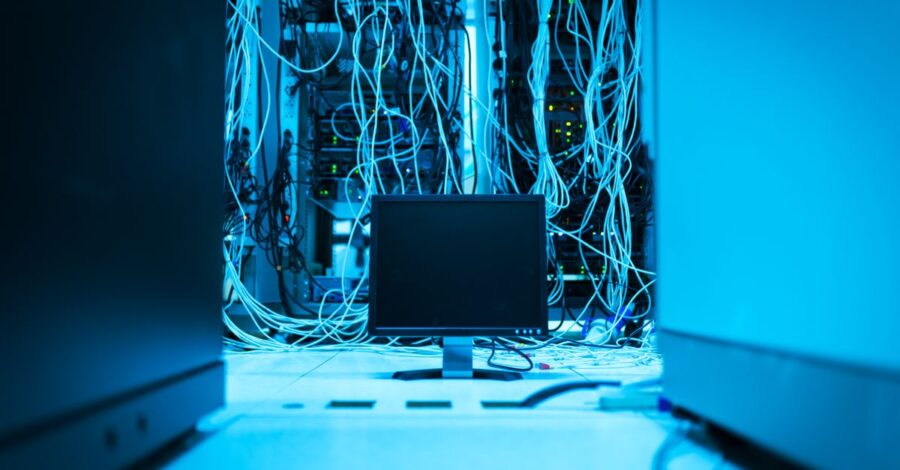 A complex network of cables in a data center with a monitor in the foreground.