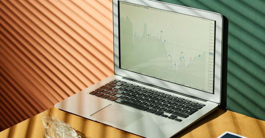 A laptop displaying analytics with financial papers on a textured surface, captured in warm lighting.